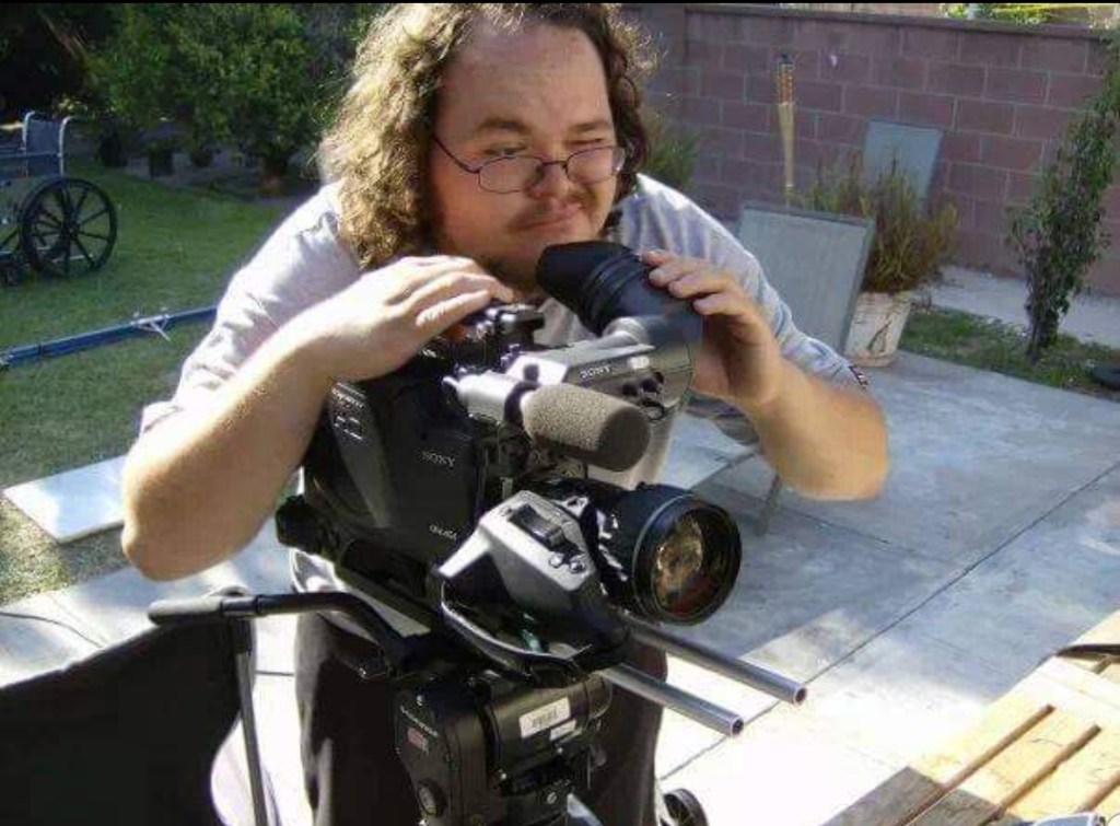 Nate leaning over a professional camera in a backyard, looking into the viewfinder.