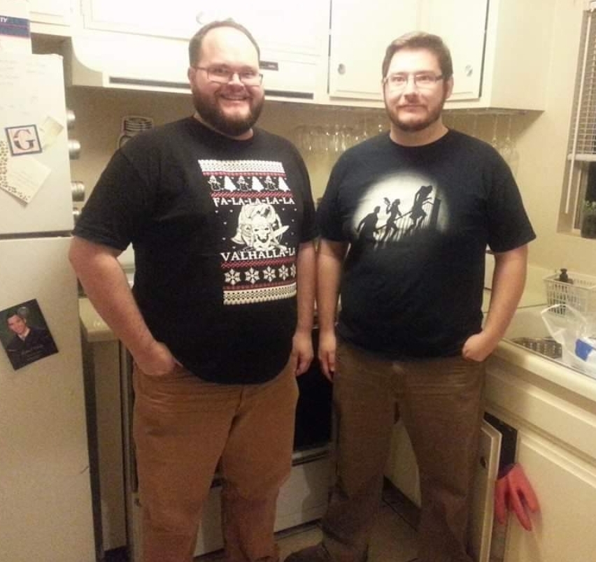 Nate standing next to Bobby, both in black graphic tees and brown dungarees.